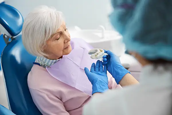 Dentist taking a silicone dental impression of a senior woman's teeth, a part of producing dental prosthetics.